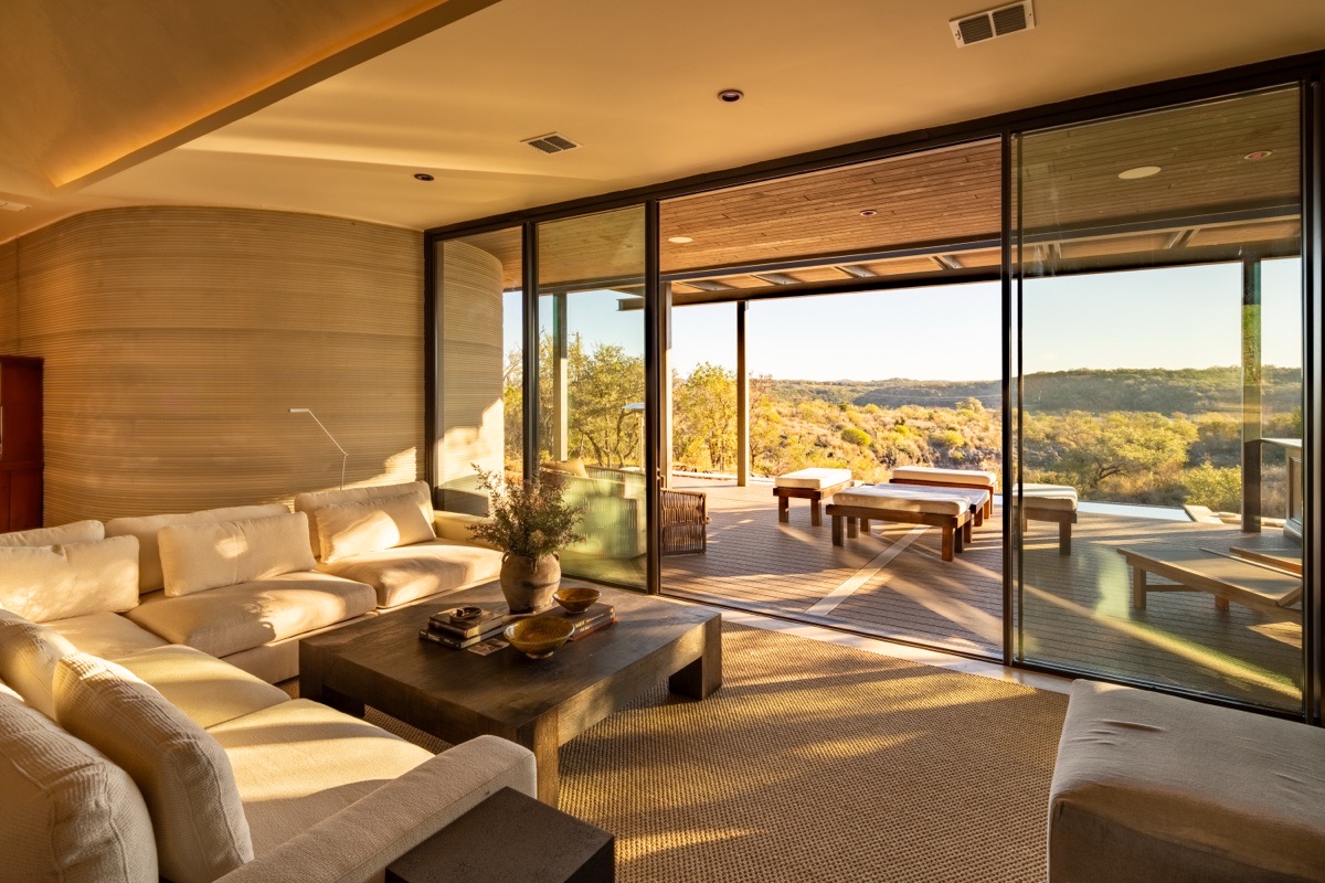 A living room opening onto a terrace and hill-country view